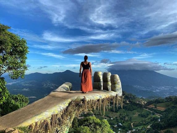 Visitor standing on a giant stone-hand viewpoint above the Antigua valley and its volcanoes