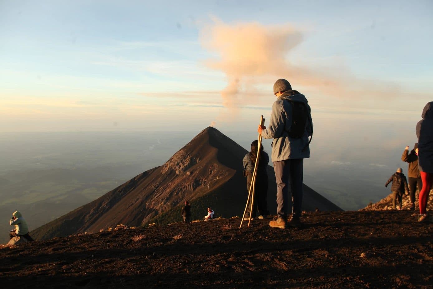 Hikers on the summit of Acatenango at sunrise, facing the smoking cone of Volcán de Fuego